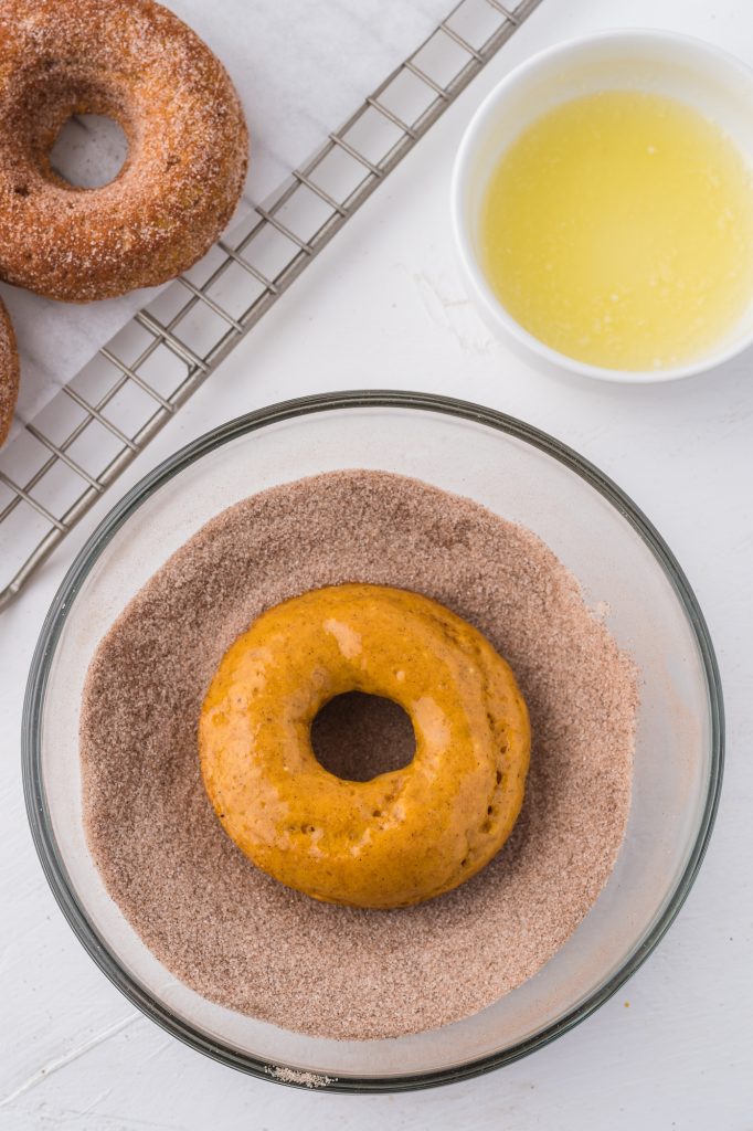 A donut in a bowl of cinnamon sugar.