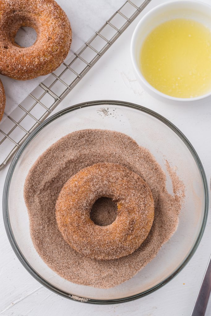 The second side of a donut in a bowl of cinnamon sugar.