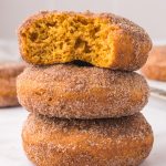 A stack of three Cinnamon Sugar Pumpkin Donuts, and the top one has a bite out of it.