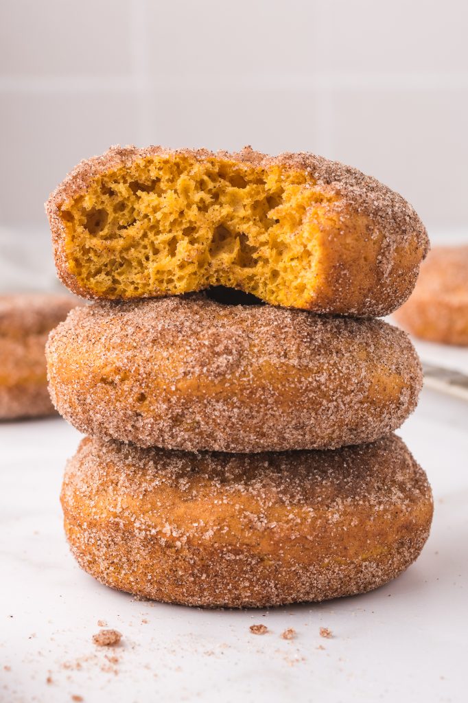 A stack of three Cinnamon Sugar Pumpkin Donuts, and the top one has a bite out of it.