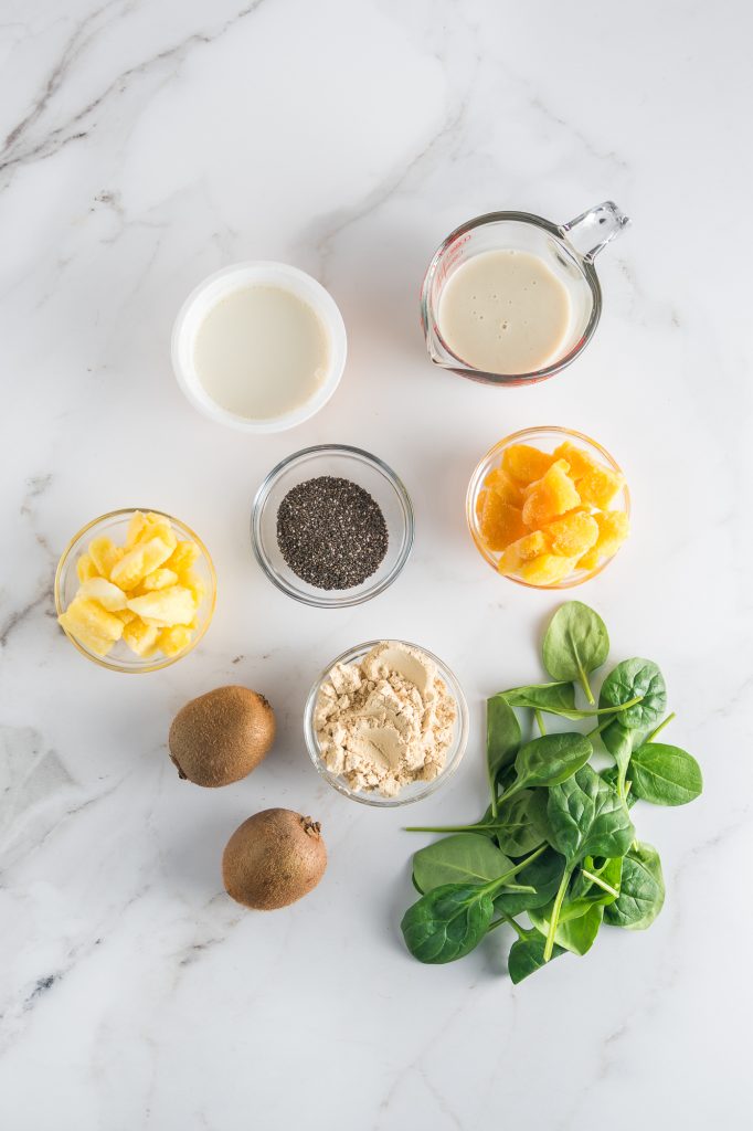 A mis-en-place of all the ingredients needed to make a Tropical Green Smoothie Bowl.