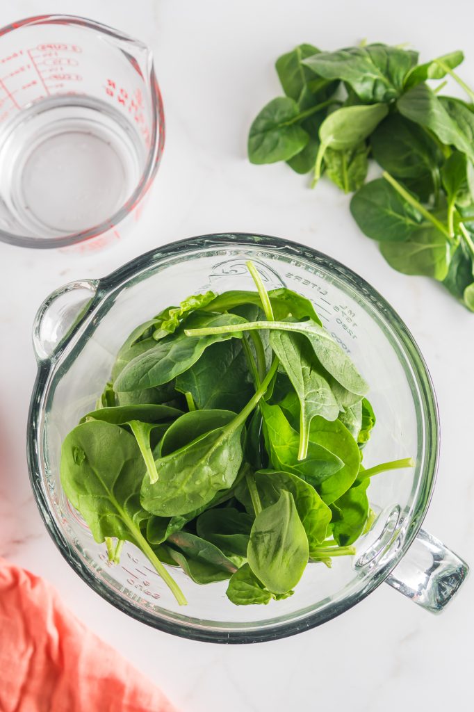 A glass blender of raw spinach.