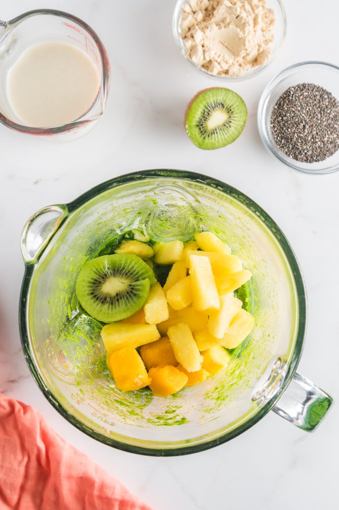 A glass blender of spinach juice topped with the other Tropical Green Smoothie Bowl base ingredients.