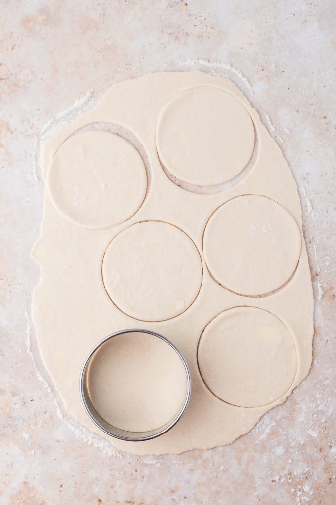 Six circles cookie cut out of some rolled out dough on a counter.