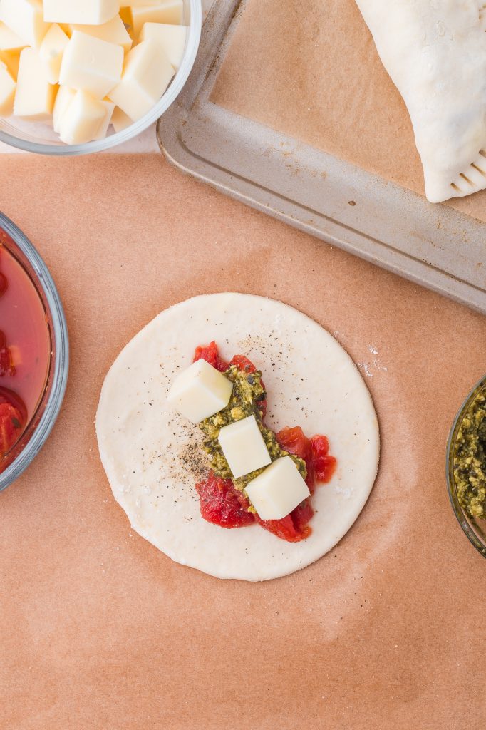 A circle of dough with tomatoes, mozzarella, and pesto on it.