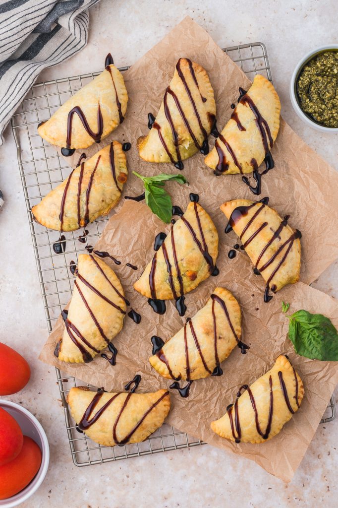 A baking sheet of baked Caprese Empanadas drizzled with balsamic glaze.