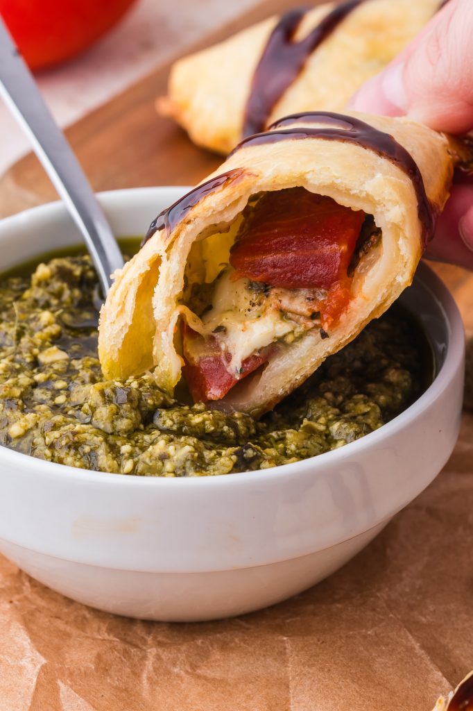 A close up of half of a Caprese Empanada being dipped into some pesto sauce.