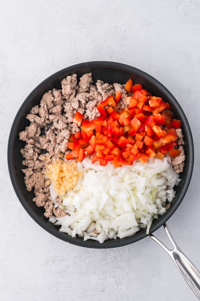 A pan of cooked ground meat, peppers, onions, and garlic in a pan in sections.