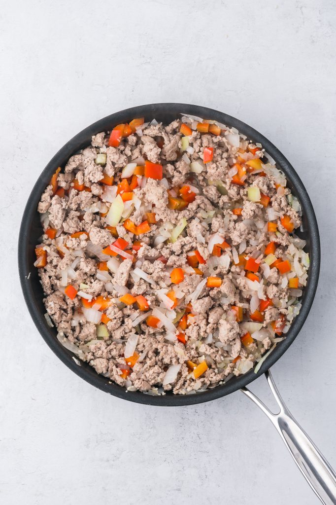 A pan of cooked ground meat, peppers, onions, and garlic in a pan mixed together