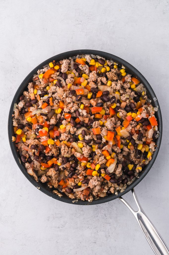 A pan of cooked ground meat, peppers, onions, garlic, corn, and black beans in a pan mixed together