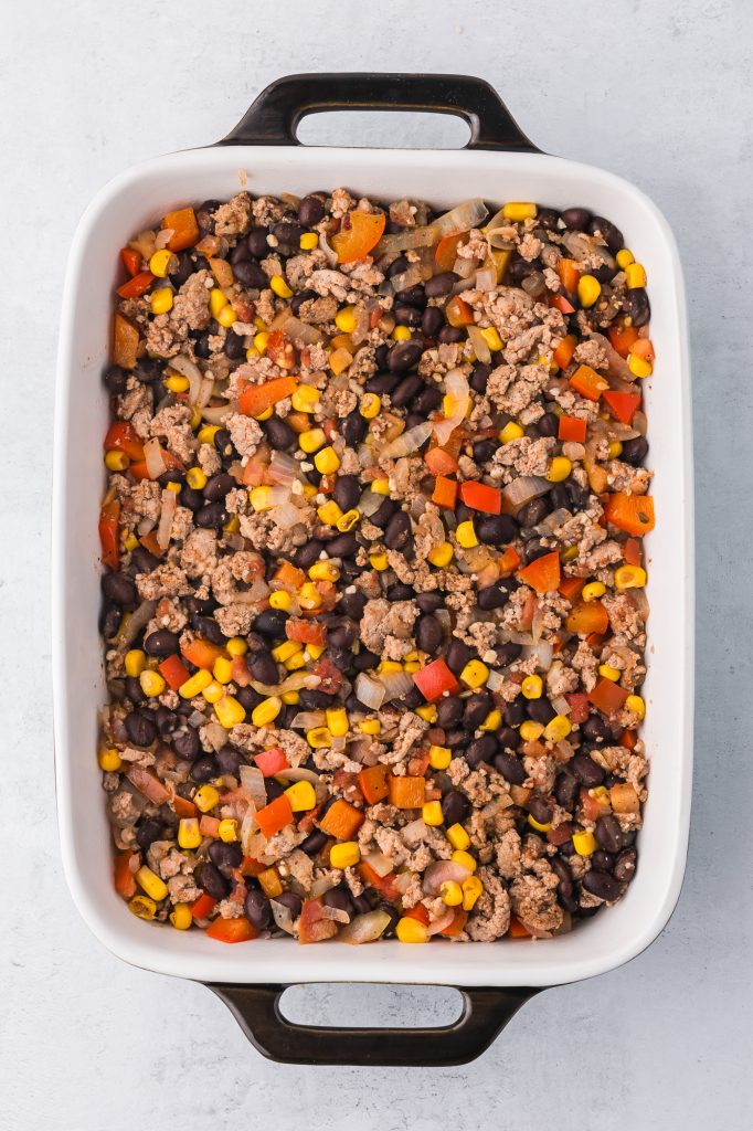 A casserole dish filled with cooked ground meat, peppers, onions, garlic, corn, and black beans.