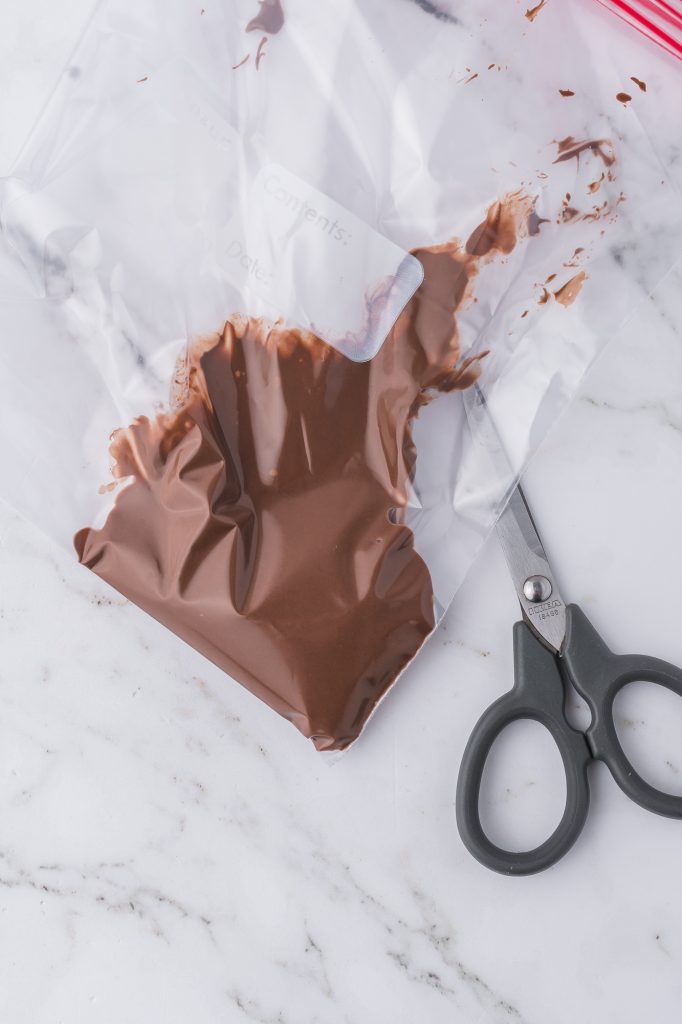 Warmed Nutella spread in a plastic piping bag with a pair of scissors under it.