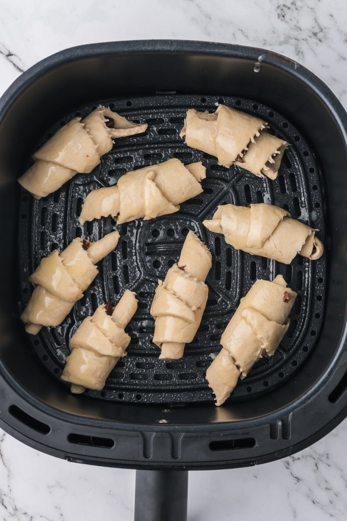 Eight raw Nutella Croissant crescents in an air fryer basket.