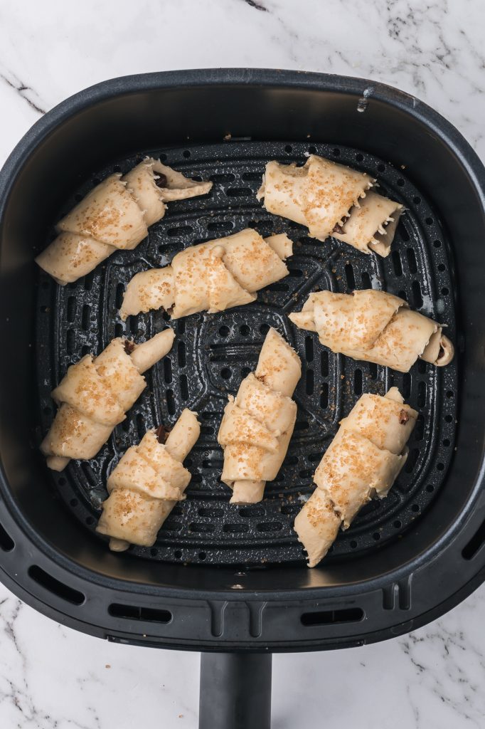 Eight raw sugar-sprinkled Nutella Croissant crescents in an air fryer basket.