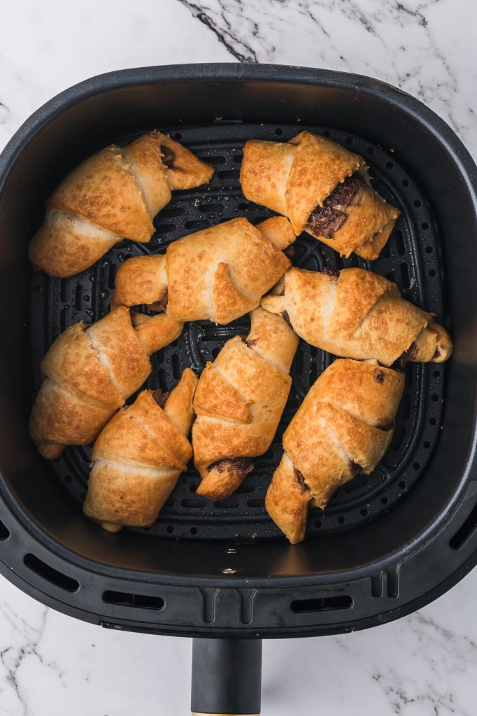 Eight baked Nutella Croissant crescents in an air fryer basket.