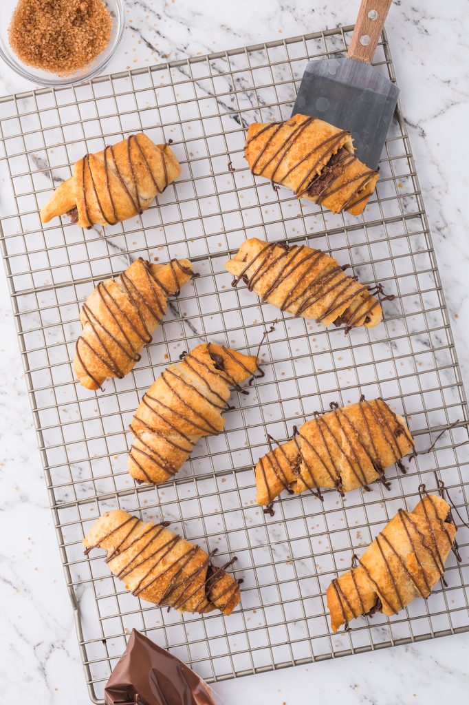 Eight Nutella-drizzled Nutella Croissants on a cooling rack.