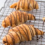 Nutella-drizzled Nutella Croissants on a metal cooling rack.