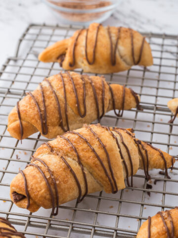 Nutella-drizzled Nutella Croissants on a metal cooling rack.