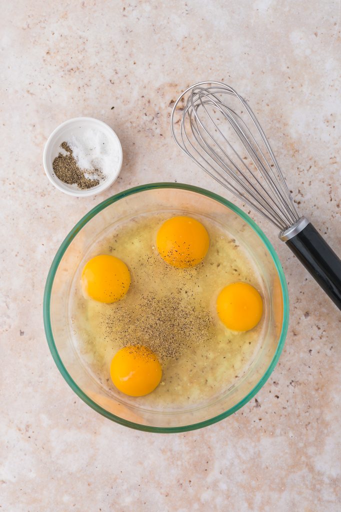 A bowl of four cracked eggs next to a whisk and some salt and pepper in a smaller bowl.