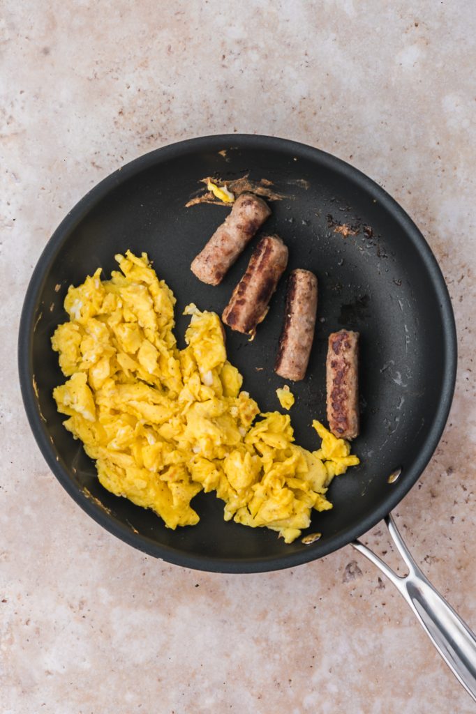 A pan with some scrambled eggs and cooked sausage.