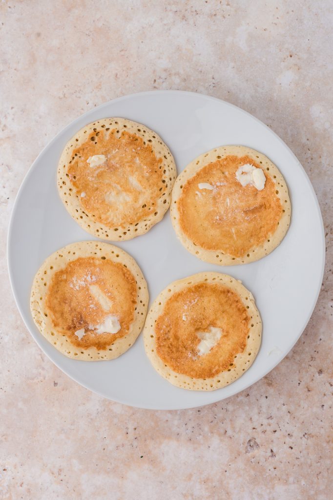 A plate with four small pancakes with butter on them.