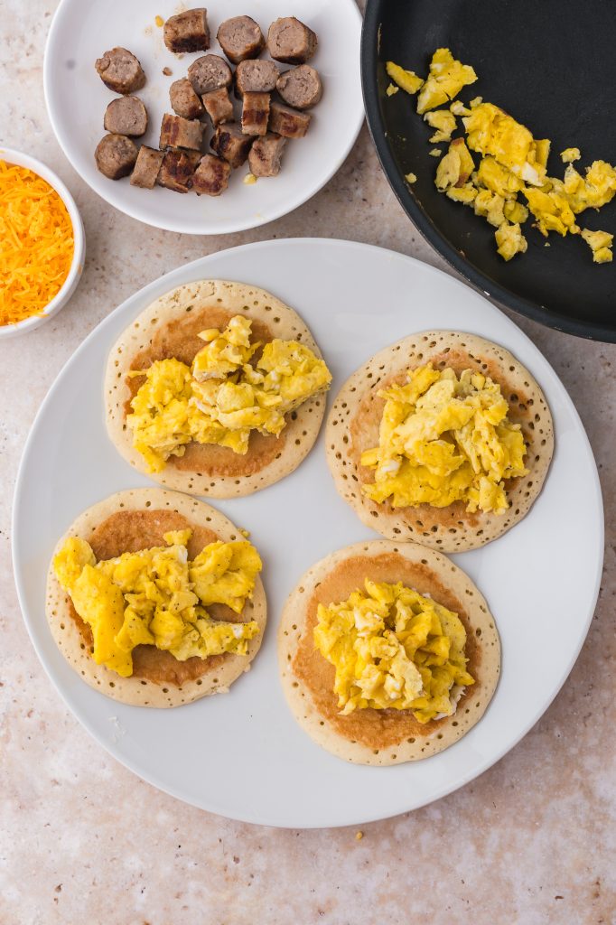 A plate of four pancakes with scrambled eggs on top.