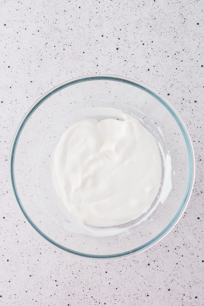 A glass bowl of whipped heavy whipping cream mixed with Greek yogurt.