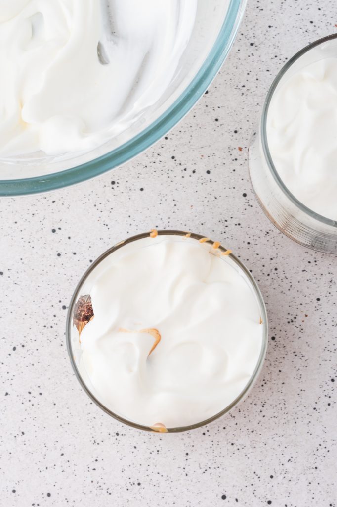 Two bowls of brownie chunks covered in warm peanut butter and whipped cream/Greek yogurt mixture next to a bowl of whipped cream/Greek yogurt mixture.