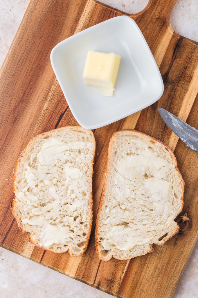 Two slices of bread with butter spread on them next to some butter in a dish.