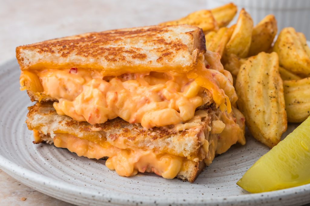 Two halves of a Pimento Grilled Cheese Sandwich stacked on a piece plate with potato wedges.