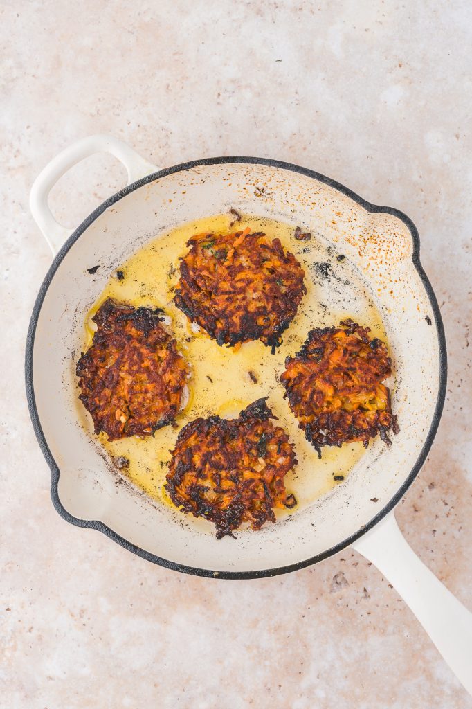 Four Sweet Potato Fritters frying in a pan.