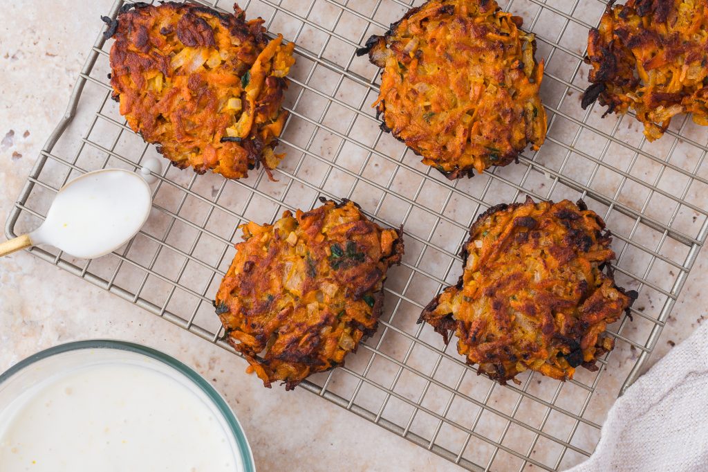 A close up of four Sweet Potato Fritters on a cooling rack with a spoon of Honey Lemon Yogurt sauce next to them.