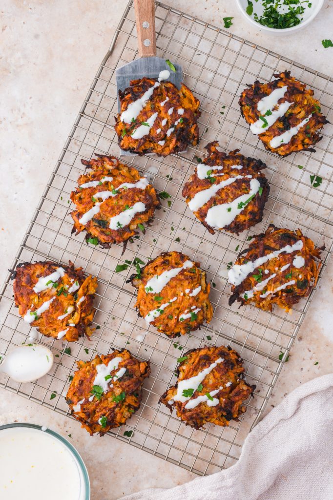 Nine Sweet Potato Fritters drizzled with Honey Lemon Yogurt sauce on a cooling rack.