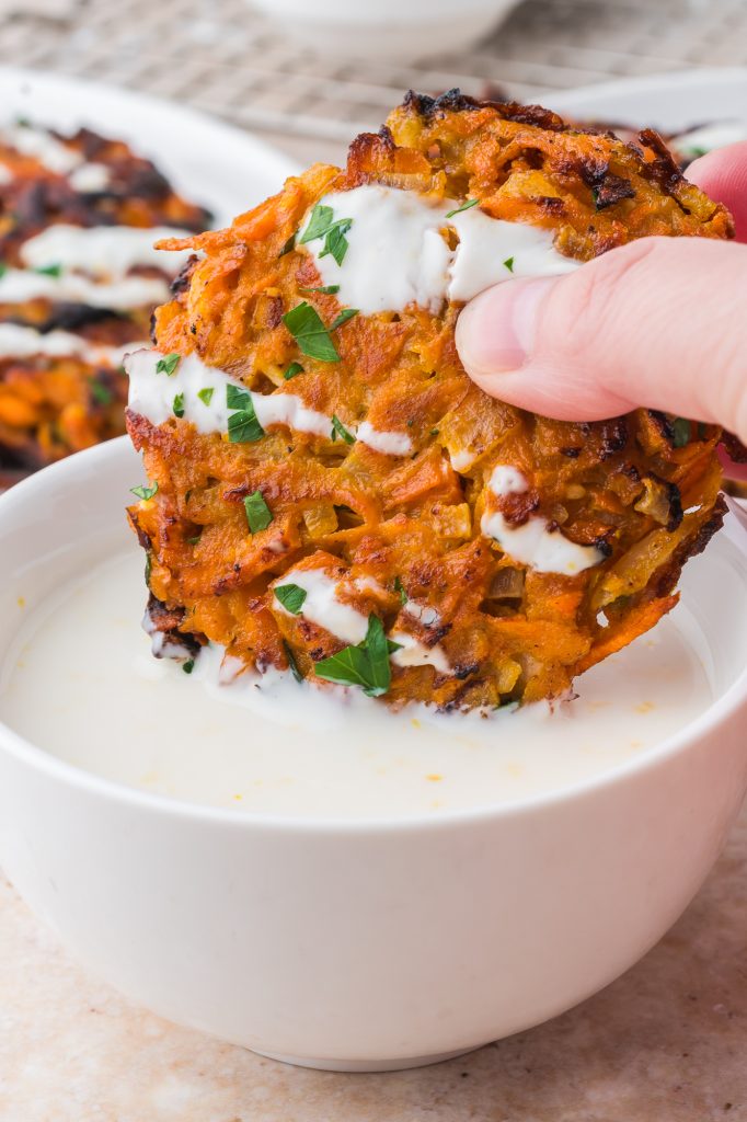 A close up of a Sweet Potato Fritter being dipped into a bowl of Honey Lemon Yogurt sauce.