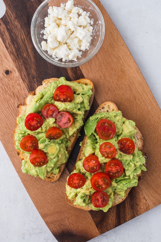 Two slices of toast spread with mashed avocado topped with sliced tomatoes.