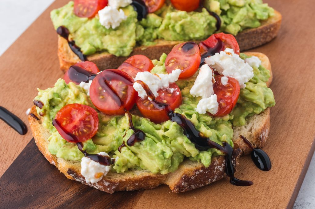 A close-up of two slices of Avocado Toast with Tomato topped with feta cheese.