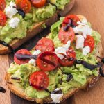 A cutting board with two pieces of Avocado Toast with Tomato.