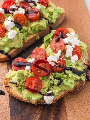 A cutting board with two pieces of Avocado Toast with Tomato.