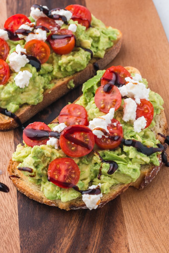 A cutting board with two pieces of Avocado Toast with Tomato.