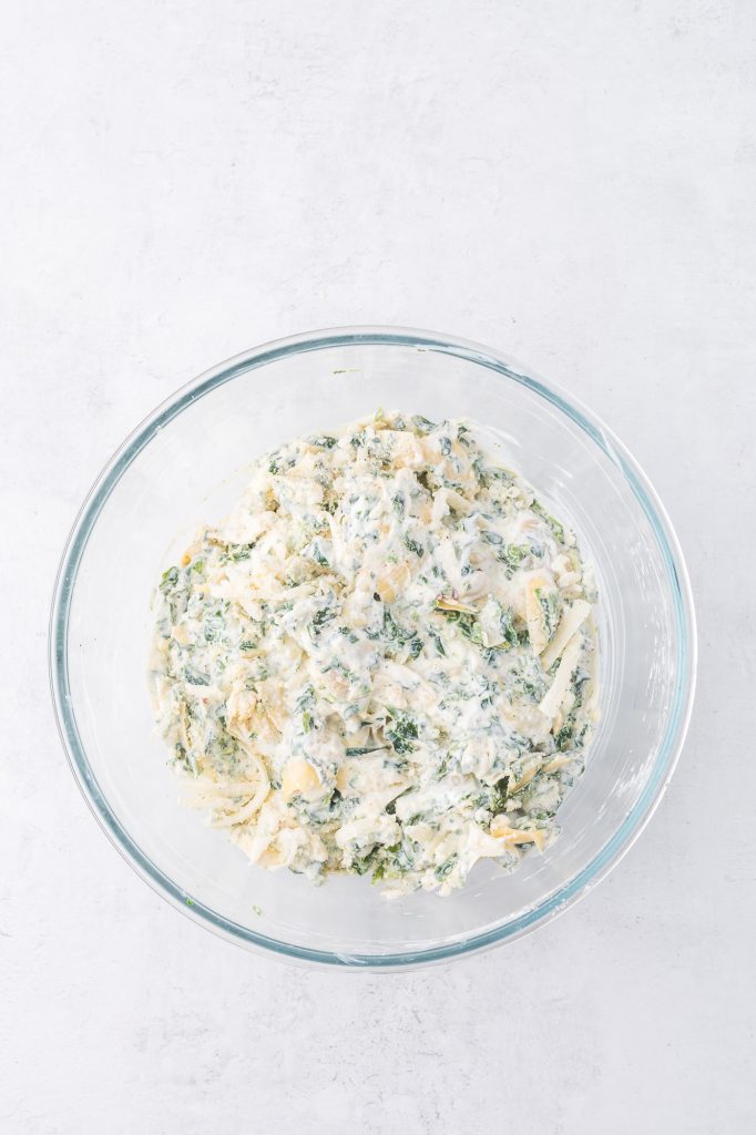 A glass bowl of the mixed ingredients for No Mayo Spinach Artichoke Dip.