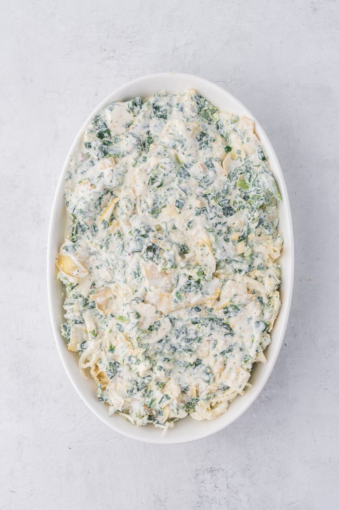 The mixed raw No Mayo Spinach Artichoke Dip spread into a casserole dish.