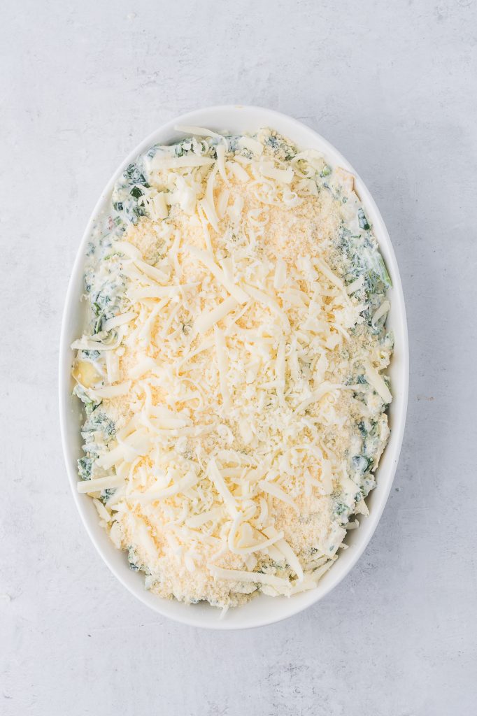 The mixed raw No Mayo Spinach Artichoke Dip spread into a casserole dish topped with cheese.