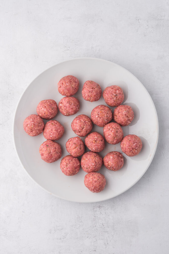 The meatball mixtures rolled into meatballs on a white plate.