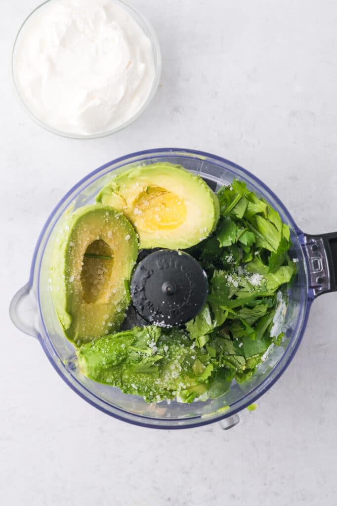 The top view of a food processor with the ingredients for the avocado lime crema prior to blending.