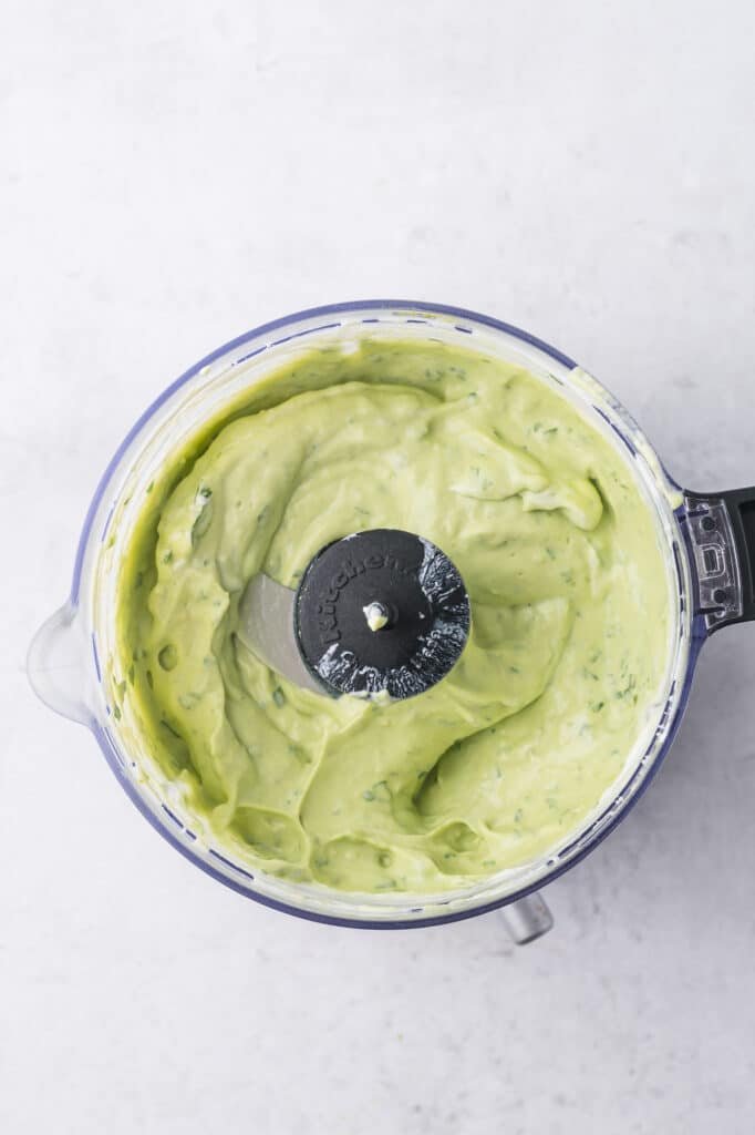 The top view of a food processor full of blended avocado lime crema.