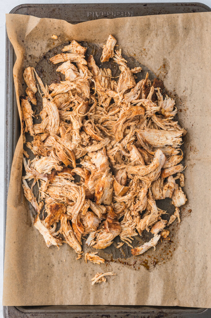 A parchment-lined tray of pulled roasted chicken breast.