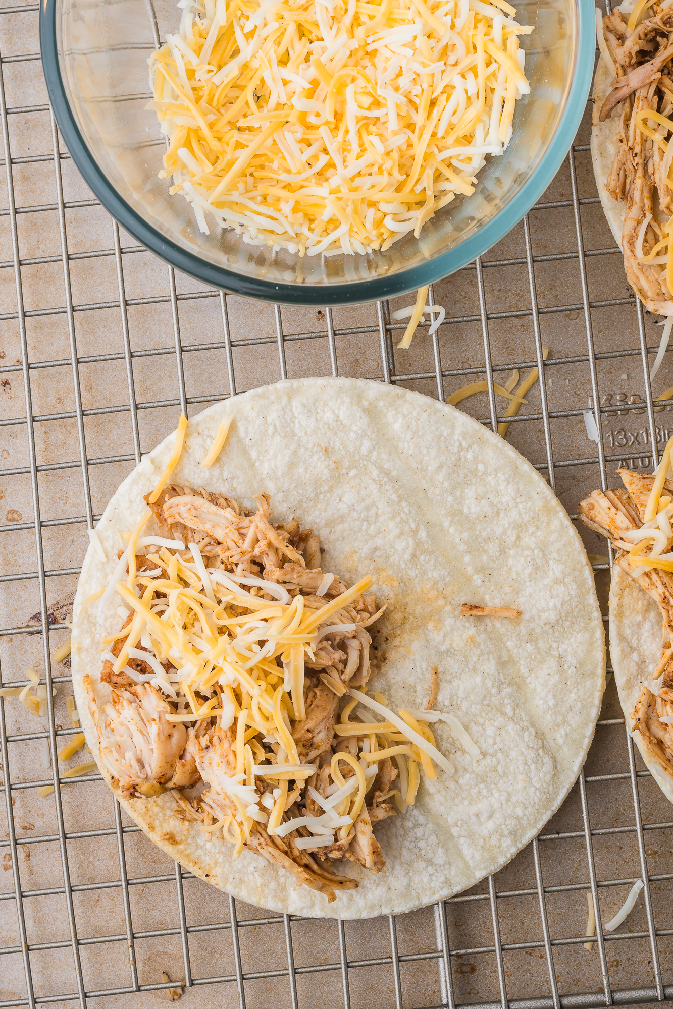 A soft taco topped with pulled chicken and shredded cheese.