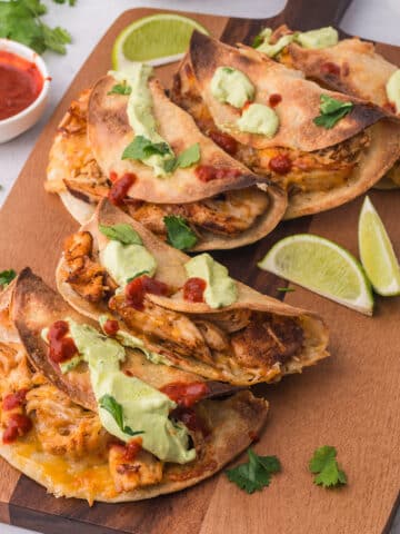 A wooden board with five Baked Chicken Tacos with Avocado Lime Crema on top.