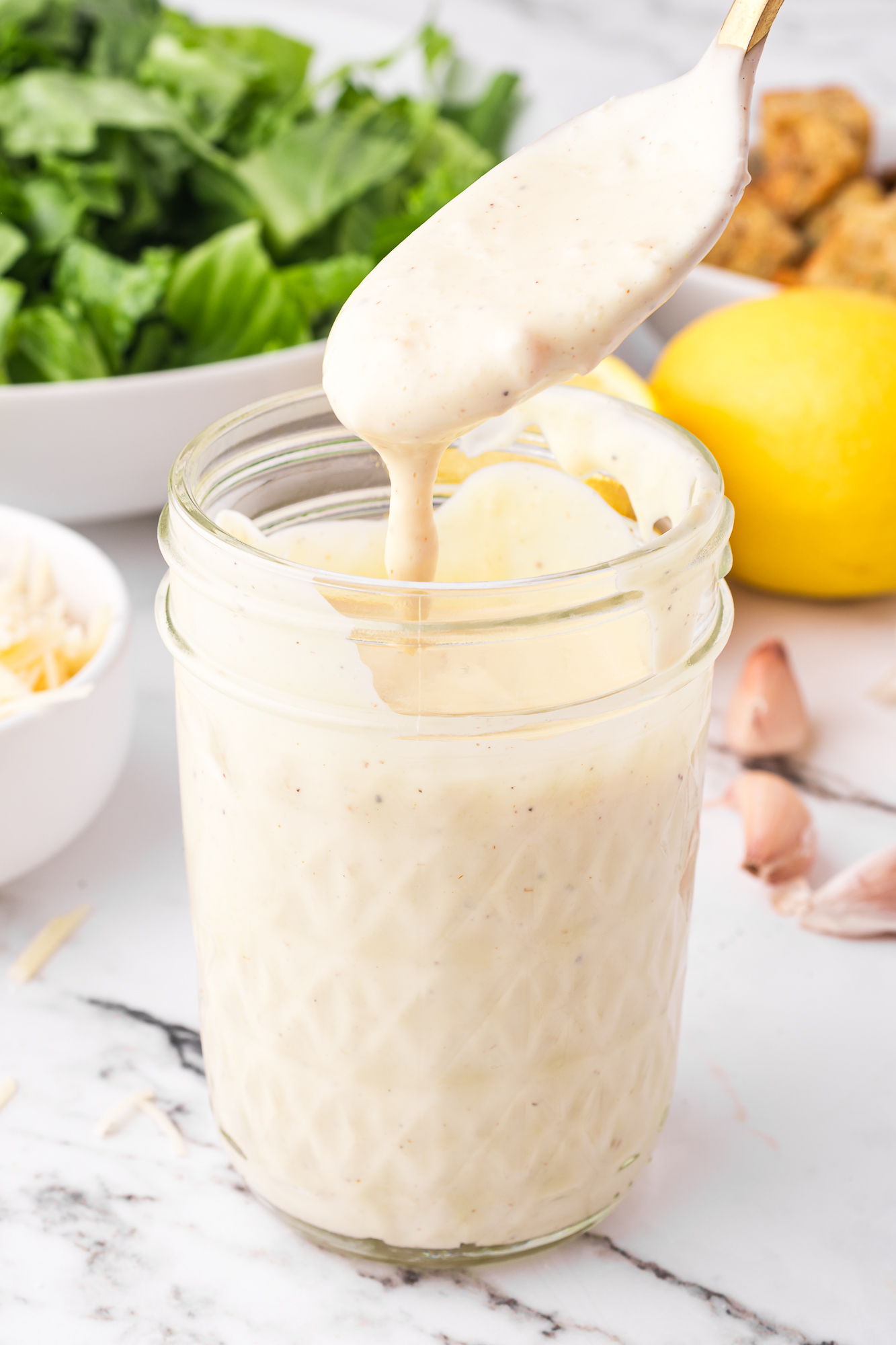 A mason jar of Homemade Caesar Dressing with a coat spoon dripping dressing back into the jar.