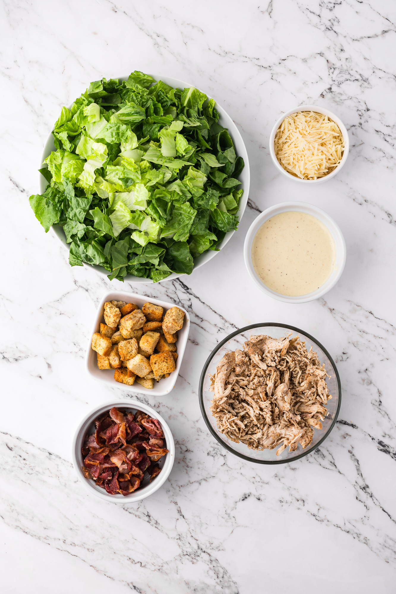 A mise en place of the ingredients for a Chicken Bacon Caesar Salad.